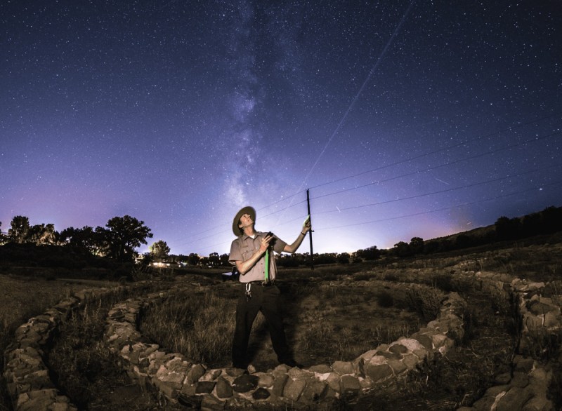 A park ranger stands inside an Ancestral Puebloan ring of stones and points his laser to a planet in the night sky at Aztec Ruins National Monument, New Mexico