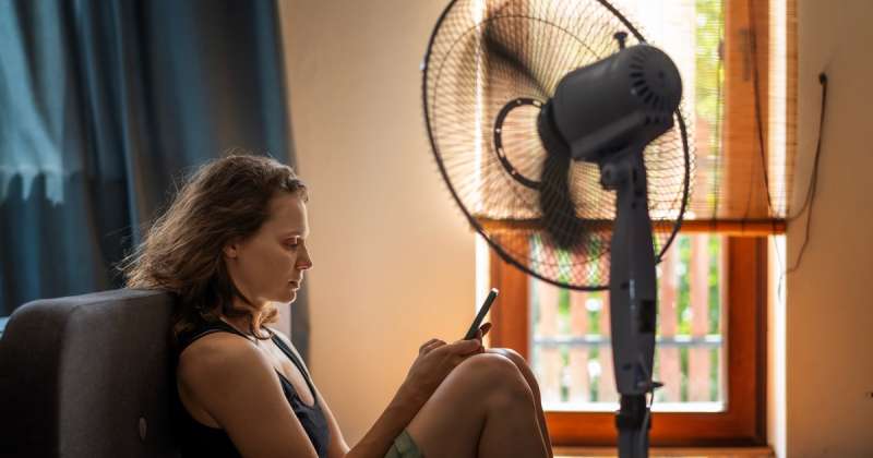 A woman sits in front of a fan to save on family expenses in New Mexico