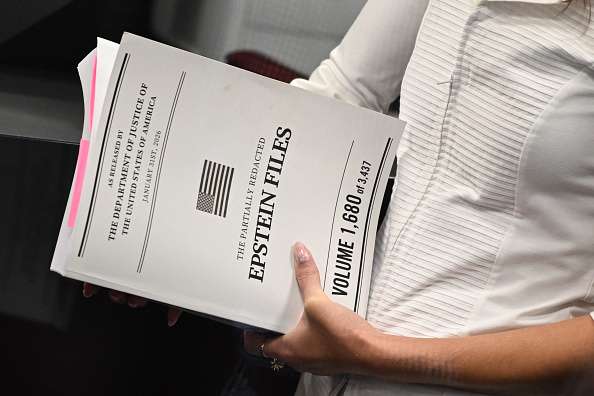 A woman holds documents titled "The Partially Redacted Epstein Files"